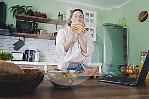 Young Caucasian smiling woman holding fresh bread in her hands while standing in the kitchen at home