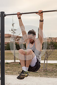 Young Caucasian sportive man doing sports on a pull-up bar