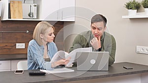 Young caucasian spouses sitting with modern laptop and documents