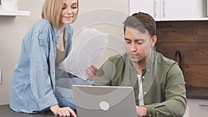 Young caucasian spouses sitting with modern laptop and documents