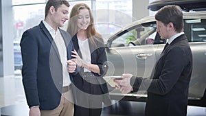 Young caucasian successful couple selecting new vehicle in car dealership. Smiling man and woman talking with sales