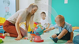 young Caucasian teacher and a little blond boy sitting on the floor and playing with the globe and other toys in