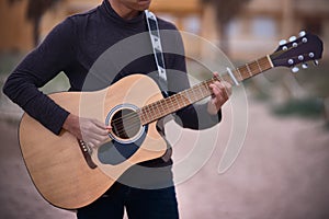 Young caucasian teenage boy playing acoustic guitar on the beach. sunglasses and dark clothing.close-up