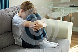 Young caucasian teenage boy sitting alone on sofa, face down crying