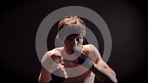 Young caucasian topless boxer boxing in front, looking at camera, jab, punch, black background 50 fps