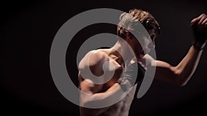 Young caucasian topless boxer boxing, jab, punch, black background, side view 50 fps