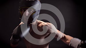 Young caucasian topless boxer boxing, jabs, turning aside, protective helmet, black background, looks at camera 50 fps