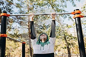 Young caucasian unshaven man 34 years old doing pull ups at the gym, unsporting non- athletic man hanging on bars on sunny autumn