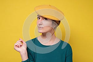 Young caucasian woamn wearing yellow beret with serious expression on face.