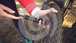 Young caucasian woman athlete tourist cyclist uses a hand tool, a bicycle pump to inflate air into a tire wheel mountain