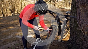 Young caucasian woman athlete tourist cyclist uses a hand tool, a bicycle pump to inflate air into a tire wheel mountain bike.