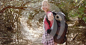 Young Caucasian woman with a backpack smiles while hiking on a woodland trail