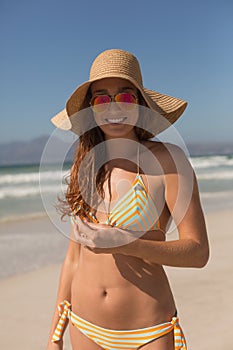 Young Caucasian woman in bikine with hat and sunglasses looking at camera on the beach
