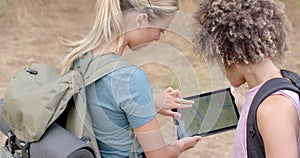 Young Caucasian woman and biracial woman are examining a tablet outdoors