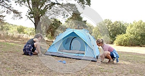 Young Caucasian woman and biracial woman set up a blue tent outdoors