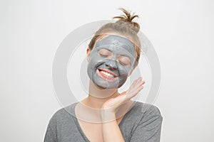 Young caucasian woman with black or grey facial clay mask on her face, smiling