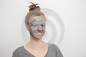 Young caucasian woman with black or grey facial clay mask on her face, smiling