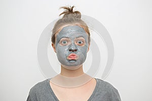 Young caucasian woman with black or grey facial clay mask on her funny face