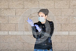Young Caucasian woman in black leather jacket and surgical mask takes on purple latex gloves