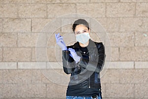 Young Caucasian woman in black leather jacket and surgical mask takes on purple latex gloves