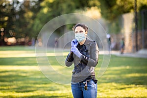 Young Caucasian woman in black leather jacket and surgical mask takes on purple latex gloves