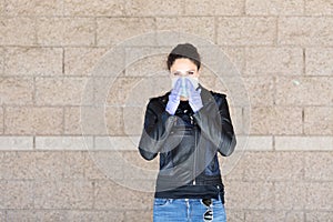 Young Caucasian woman in black leather jacket and surgical mask takes on purple latex gloves