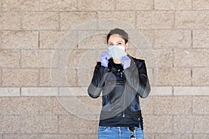 Young Caucasian woman in black leather jacket and surgical mask takes on purple latex gloves