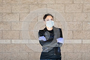 Young Caucasian woman in black leather jacket and surgical mask takes on purple latex gloves