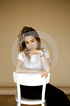 young caucasian woman in black pants and a white T-shirt sitting on a chair, portrait of a brown-eyed brunette with