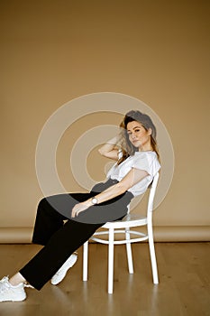 young caucasian woman in black pants and a white T-shirt sitting on a chair, portrait of a brown-eyed brunette with