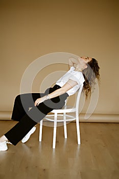 young caucasian woman in black pants and a white T-shirt sitting on a chair, portrait of a brown-eyed brunette with