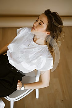 young caucasian woman in black pants and a white T-shirt sitting on a chair, portrait of a brown-eyed brunette with