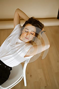 young caucasian woman in black pants and a white T-shirt sitting on a chair, portrait of a brown-eyed brunette with