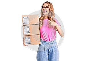 Young caucasian woman with blond hair holding delivery package smiling happy pointing with hand and finger