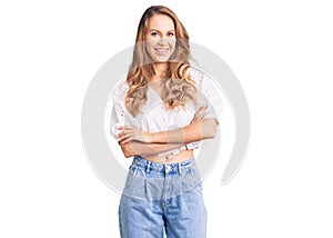 Young caucasian woman with blond hair wearing elegant summer tshirt happy face smiling with crossed arms looking at the camera
