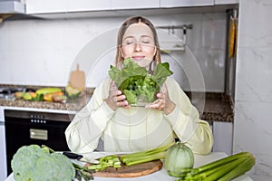 Young caucasian woman with blonde hair making detox salad with fresh green vegetables on kitchen at home