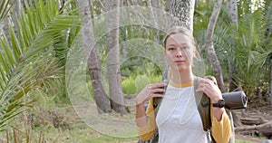 A young Caucasian woman with blonde hair stands in a forest setting with copy space