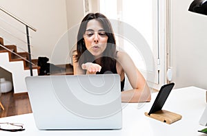 Young caucasian woman blowing a kiss goodbye during video call with a friend at home.