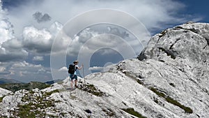 Young Caucasian woman in blue dress wearing a hiking backpack climbing a limestone white mountain peak