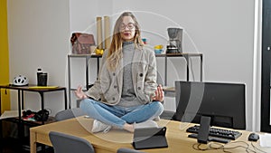 Young caucasian woman business worker doing yoga exercise sitting on table at office