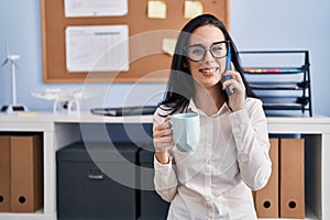 Young caucasian woman business worker talking on smartphone drinking coffee at office
