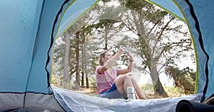 Young Caucasian woman captures a moment with her phone inside a tent