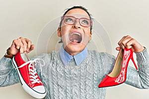 Young caucasian woman choosing high heel shoes and sneakers angry and mad screaming frustrated and furious, shouting with anger
