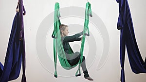 Young caucasian woman climbs in hammock in studio indoors. Aerial aero fly fitness trainer workout. Pose of Lotus