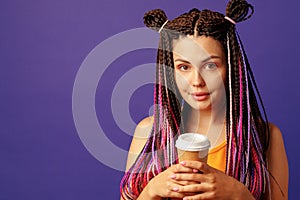 Young caucasian woman with colorful long cornrows holding a cup of coffee against purple background