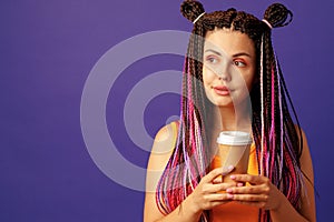 Young caucasian woman with colorful long cornrows holding a cup of coffee against purple background