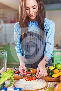 Young Caucasian woman cooking in the kitchen, making a cake, decorating it with strawberry