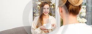 The young caucasian woman with a cup of coffee has an appointment with a female doctor beautician in the hospital office