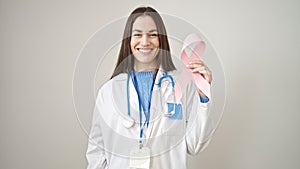Young caucasian woman doctor holding breast cancer awareness pink ribbon over isolated white background