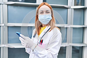 Young caucasian woman doctor wearing medical mask using smartphone at hospital